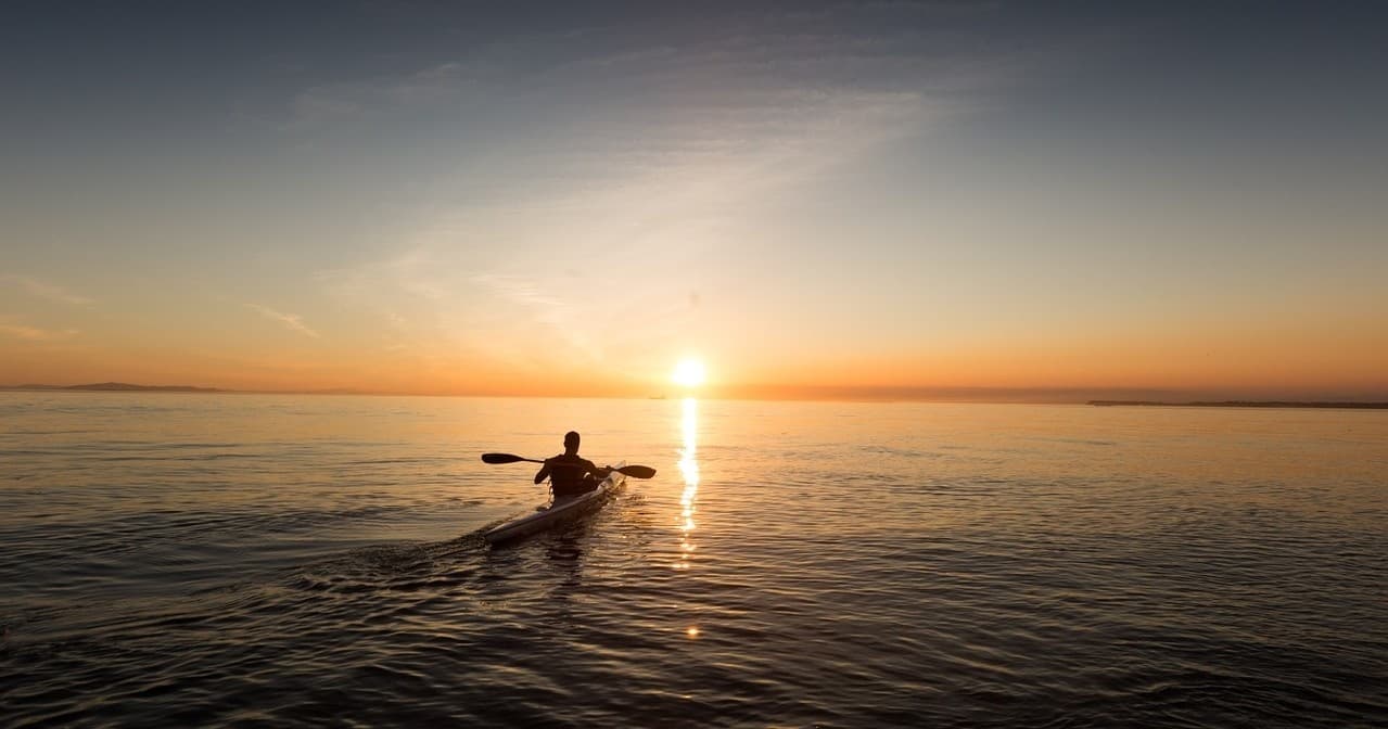 Kayaker paddling at sunrise on calm open ocean, silhouetted