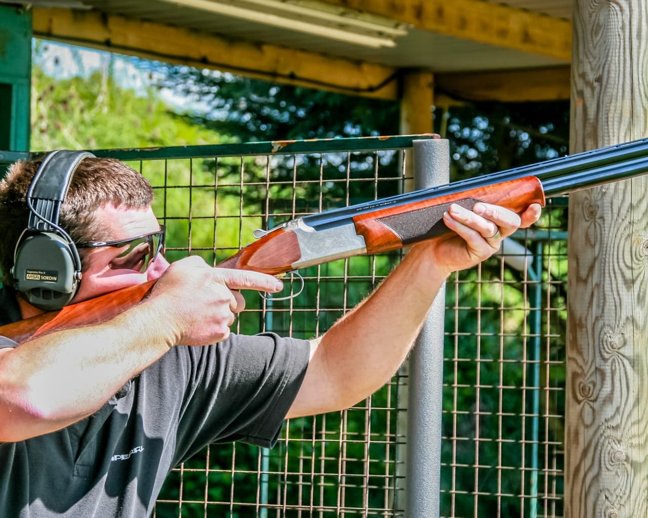 Shooter breaking clay targets at outdoor shotgun range field