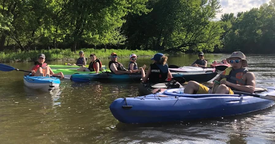 Group of kayakers paddling a calm tree-lined river on sunny day