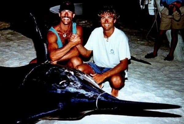 Two anglers posing with large swordfish on sandy beach at night