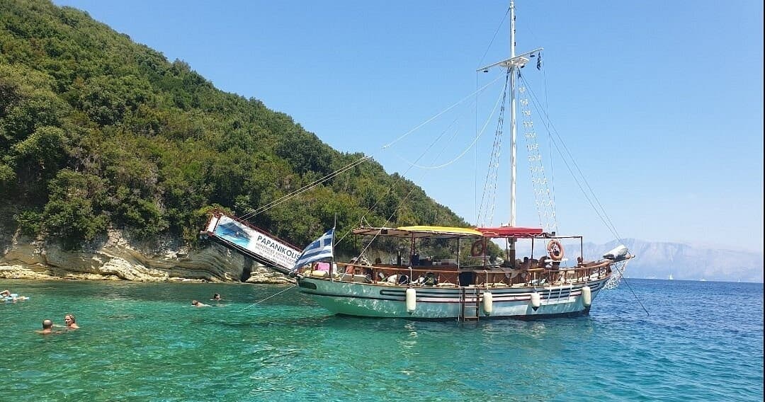 Wooden cruise boat anchored in clear turquoise water by rocky coast