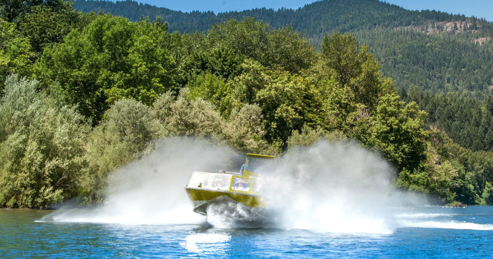 White-water jet boat creating massive spray on tree-lined mountain river