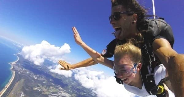 Tandem skydivers freefalling over coastal landscape and clouds