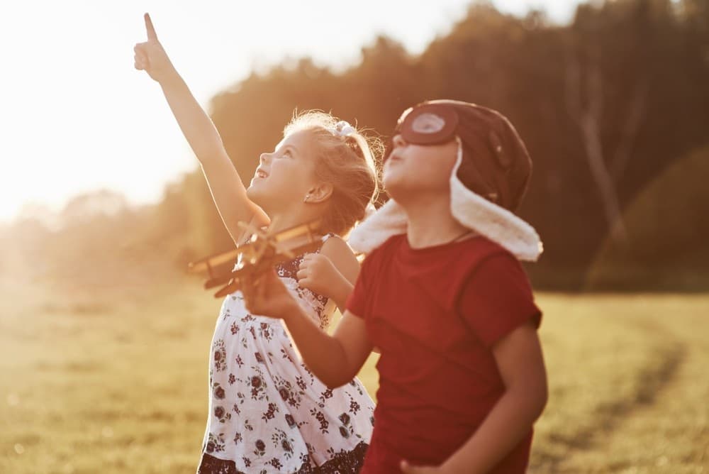 Children playing with toy airplane in sunlit field pointing upward