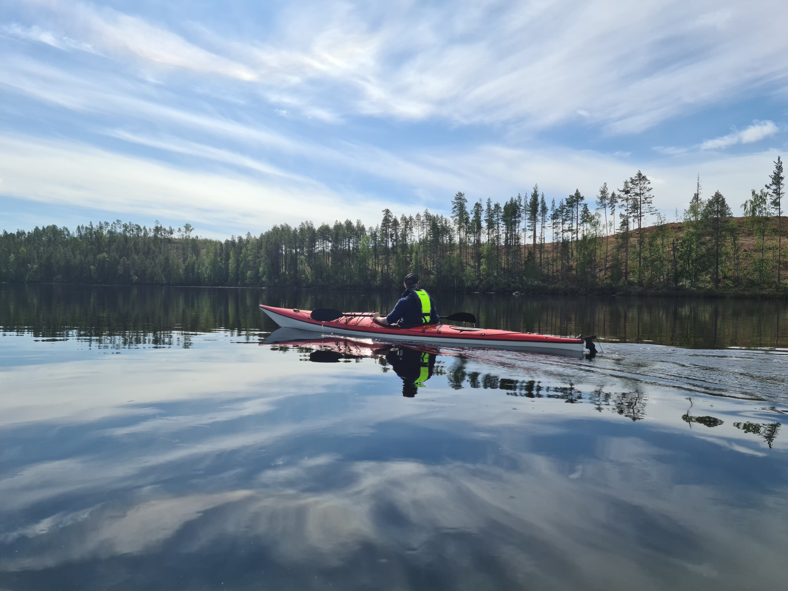 Solo kayaker paddling across glassy lake at dawn in Lapland