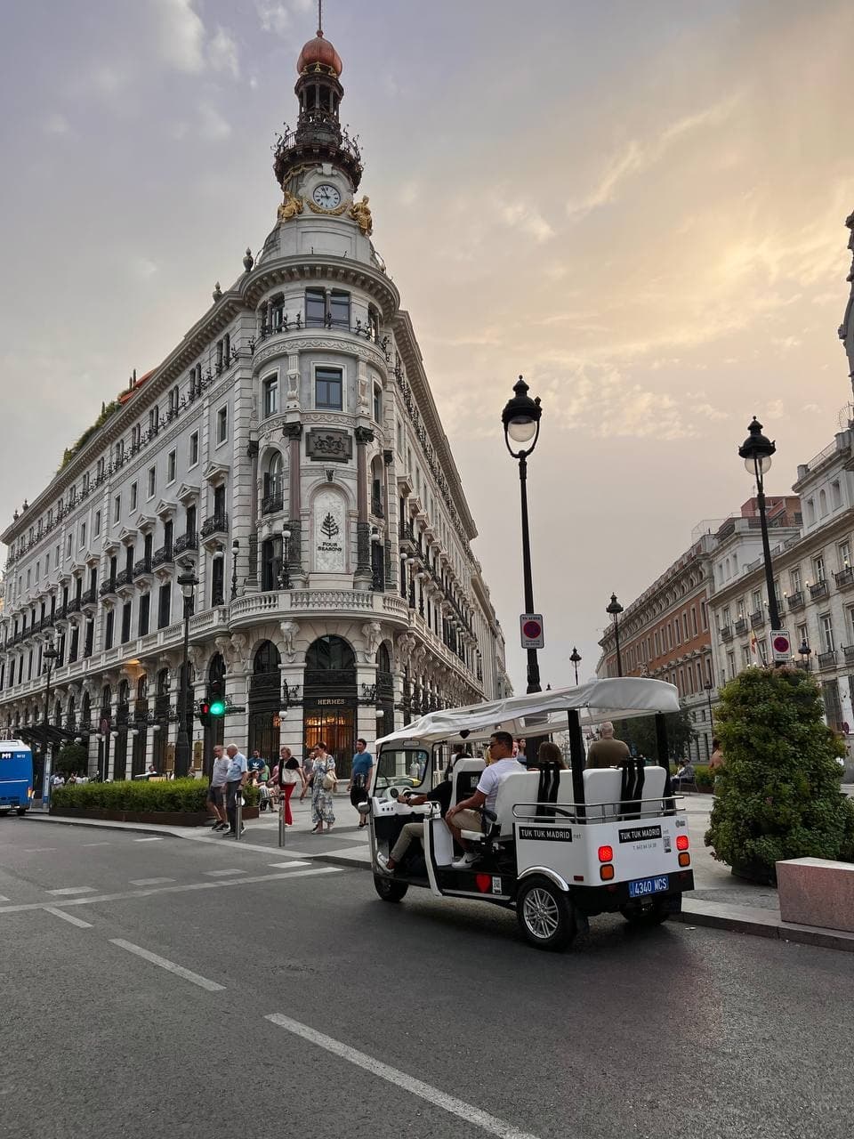 Tuk-tuk driving past Gran Vía architecture during Madrid sunset tour