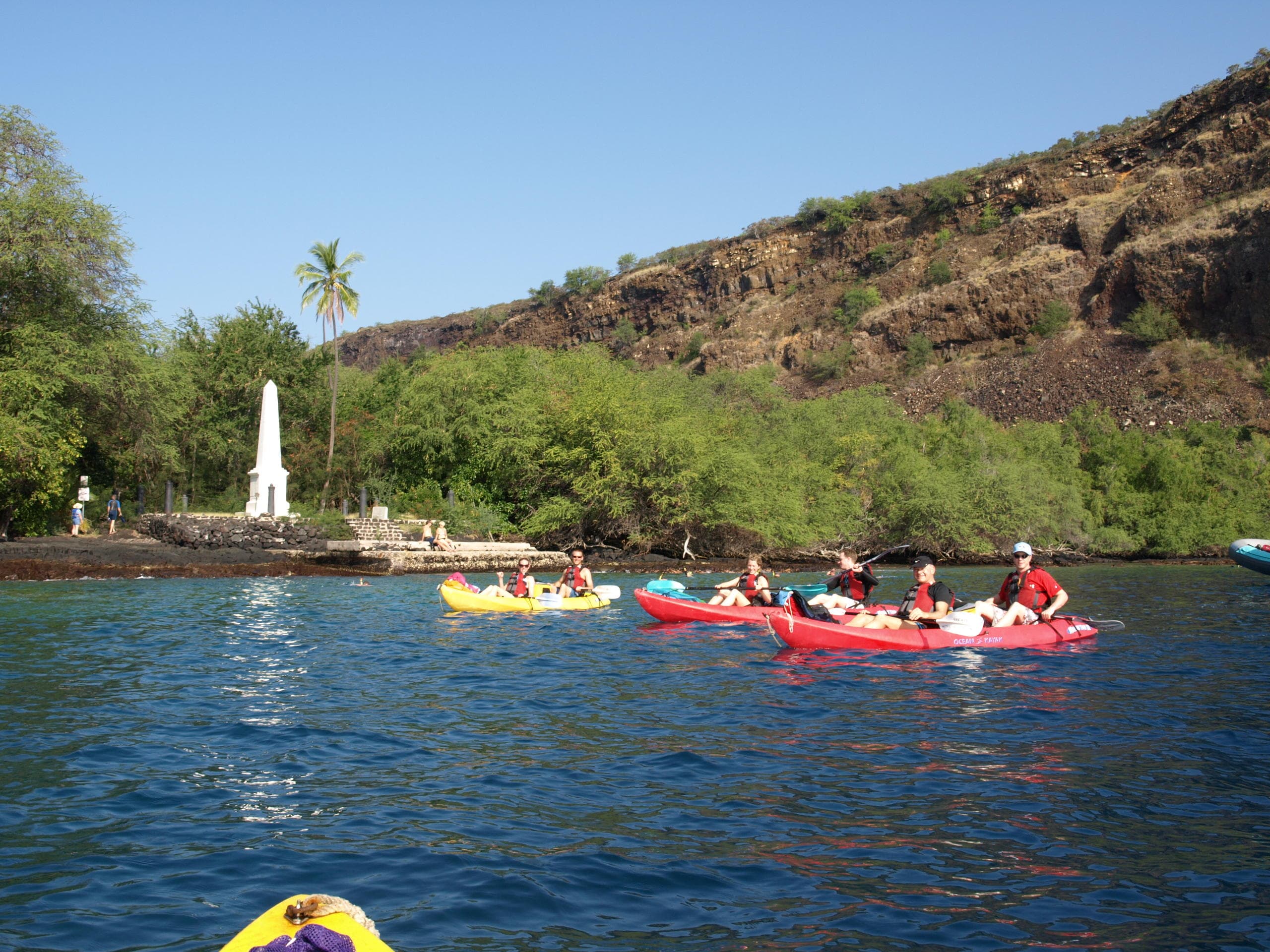 Group kayaking along volcanic coastline under bright blue skies