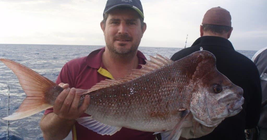 Fisherman posing with large snapper aboard boat on open ocean