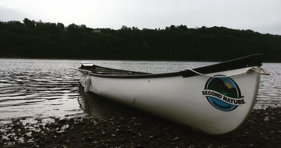 White canoe pulled ashore at calm lake edge under overcast sky