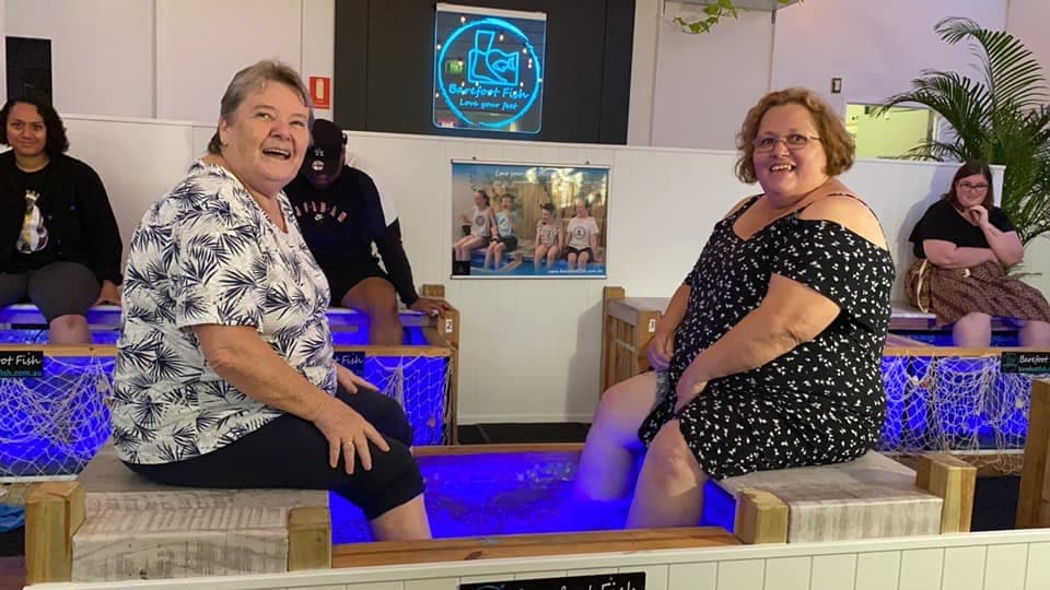 Two women laughing during indoor fish pedicure session bench