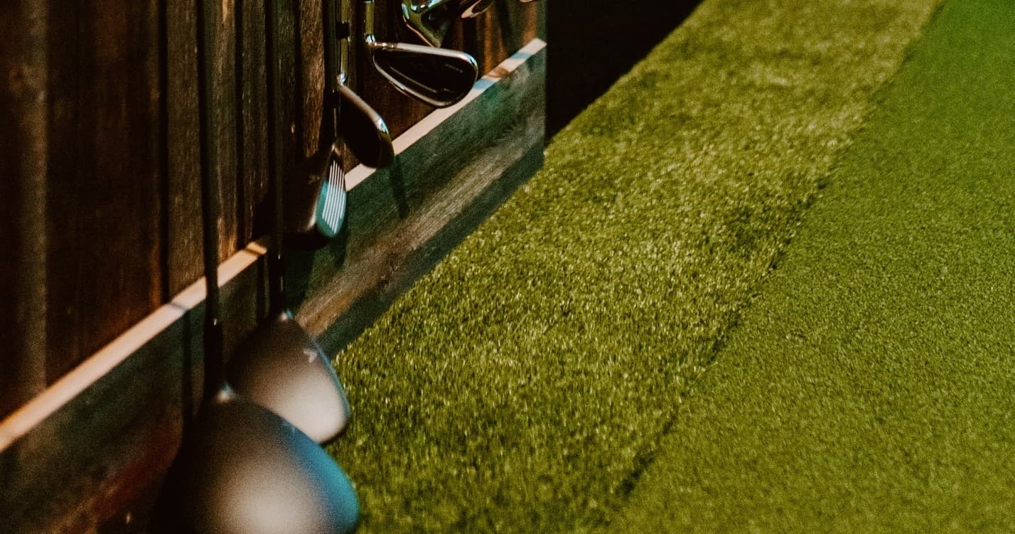Close-up golf clubs on indoor turf practice mat at bay