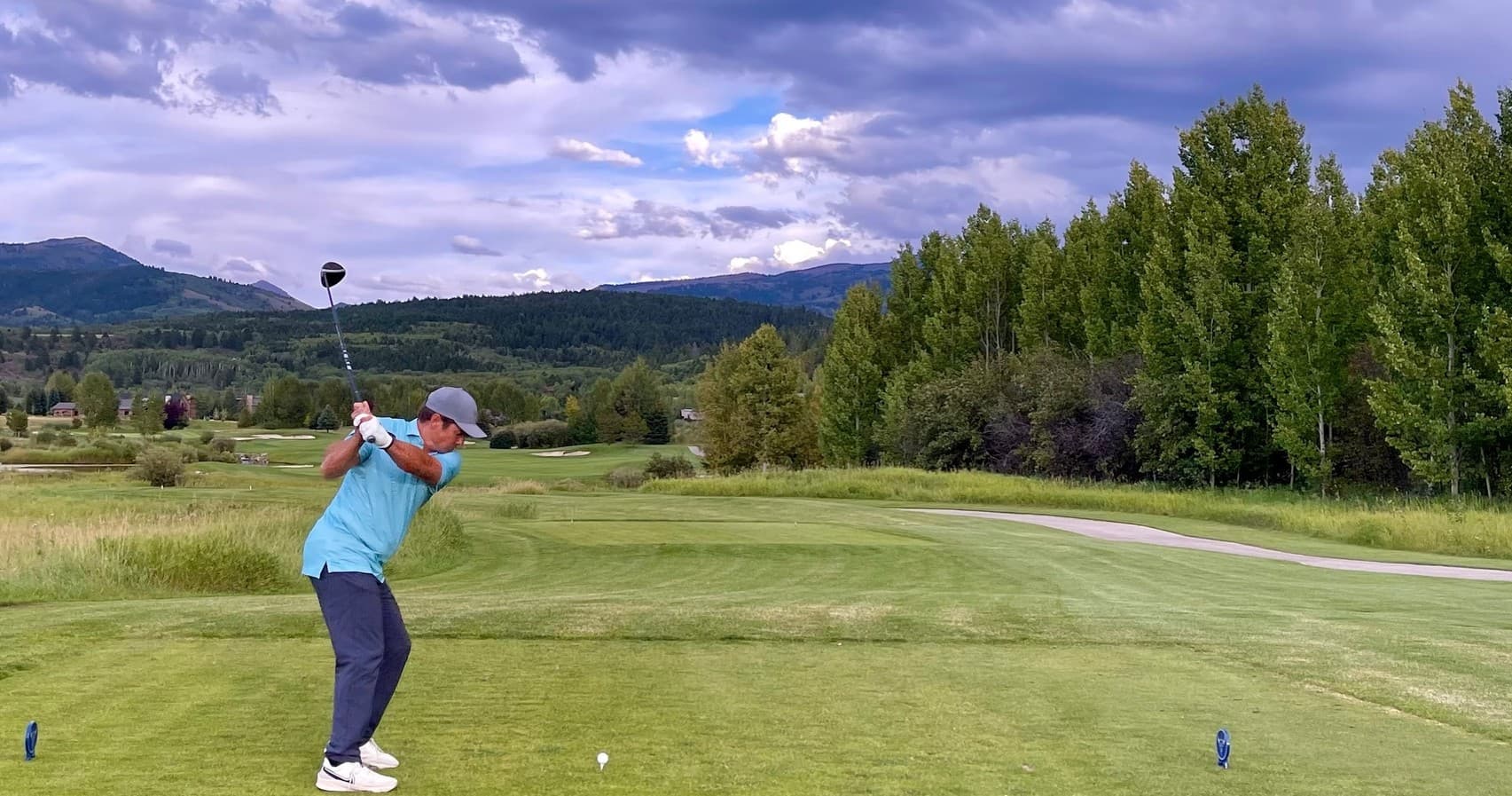 Golfer teeing off on scenic mountain golf course under clouds