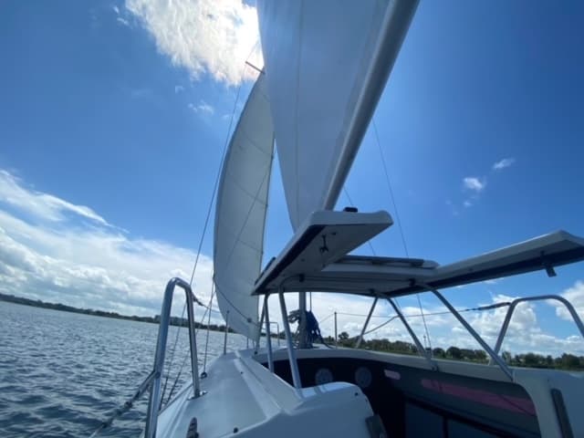 Sailboat cockpit and full sails under blue sky, daytime sail