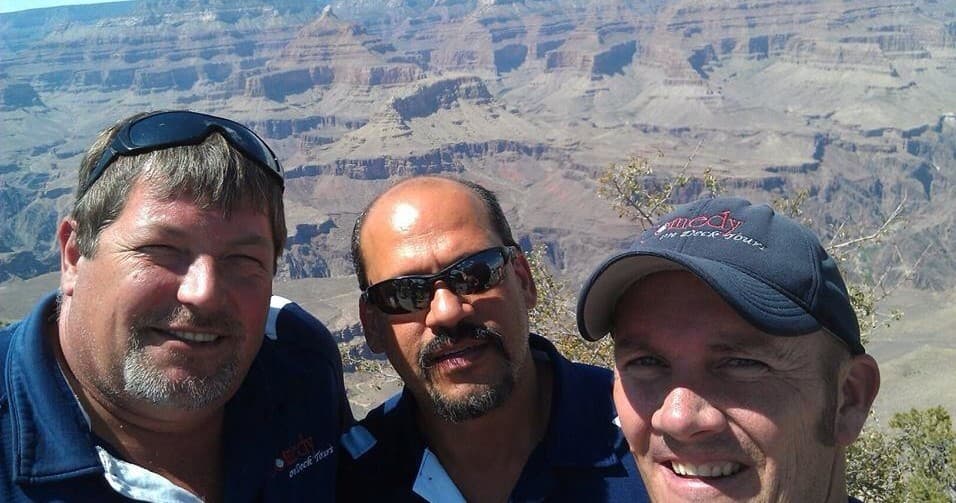 Three men posing at Grand Canyon rim on scenic lookout selfie