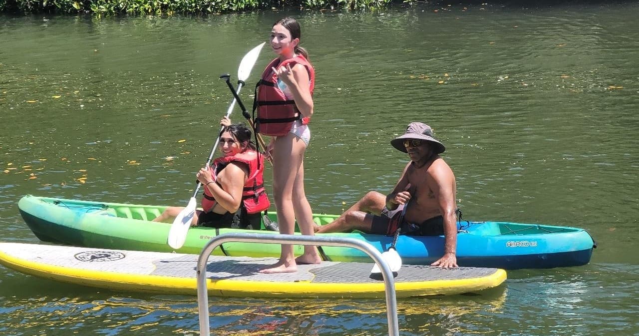 Stand-up paddleboarding family on calm lake near greenery