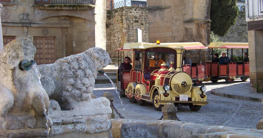 Tourist road train near stone fountain exploring old town square