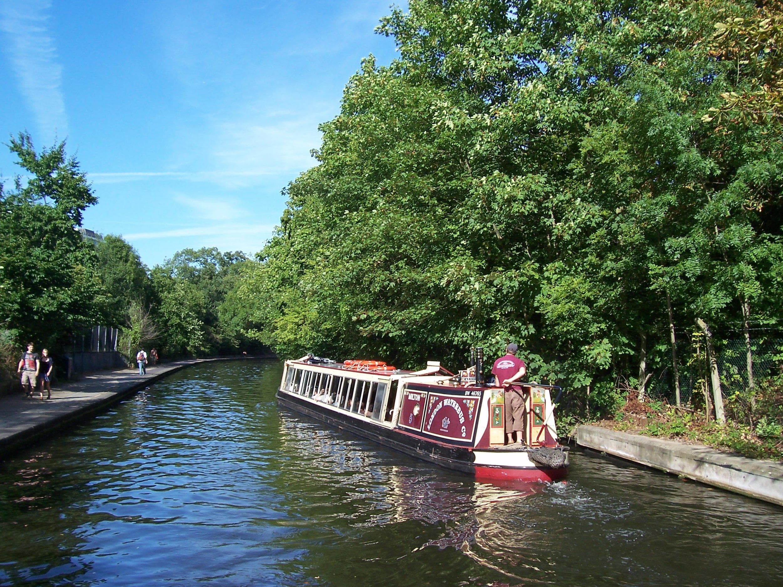 Narrowboat cruising tree-lined London canal for sightseeing