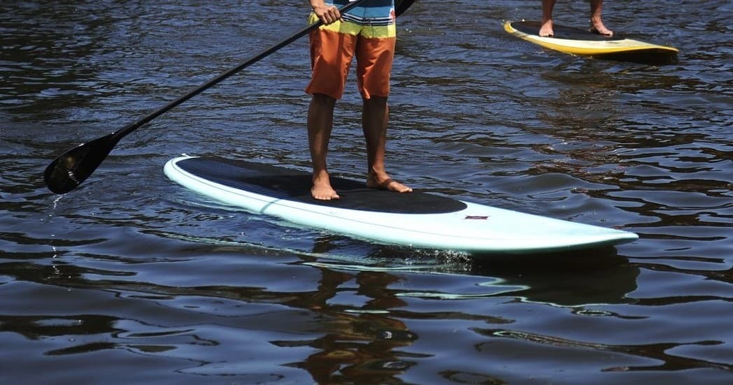 Stand-up paddleboarder on lake, close-up of board and paddle