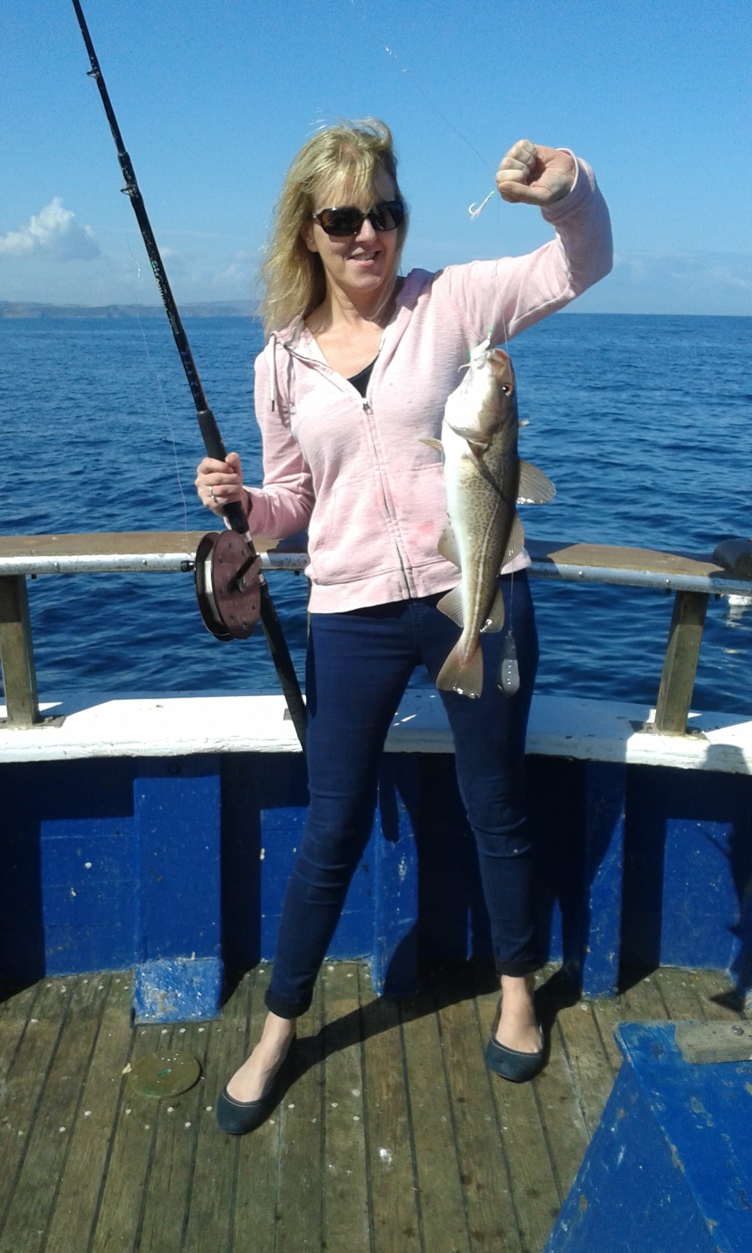 Woman holding caught fish on sunny sea angling trip
