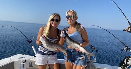 Two women holding fish on sportfishing boat in open ocean