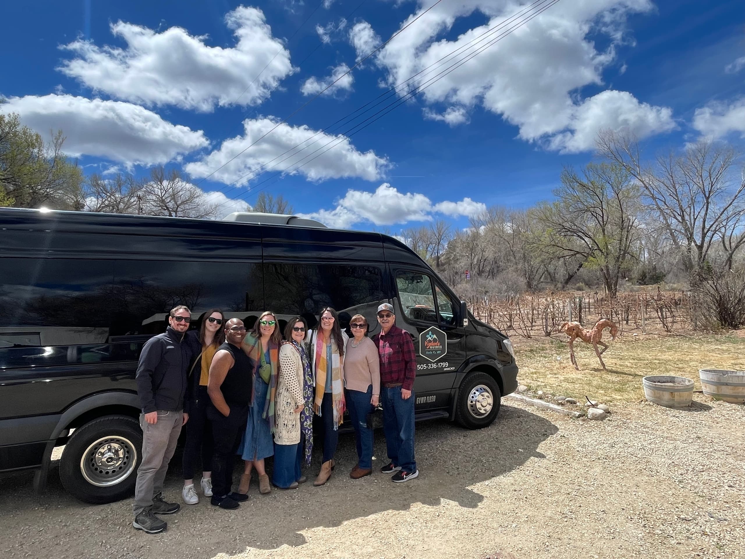 Tour group posing by black adventure van in rural desert