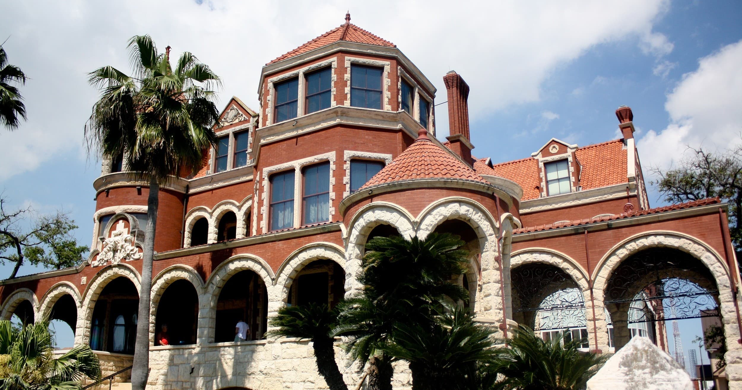 Historic seaside mansion exterior with arched verandas and palms