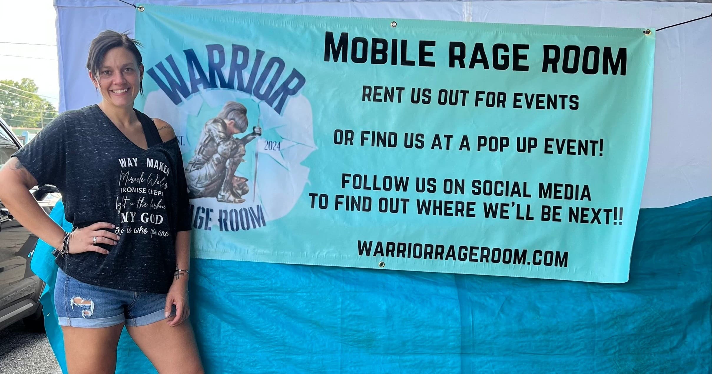 Woman with Warrior Rage Room banner at outdoor pop-up tent