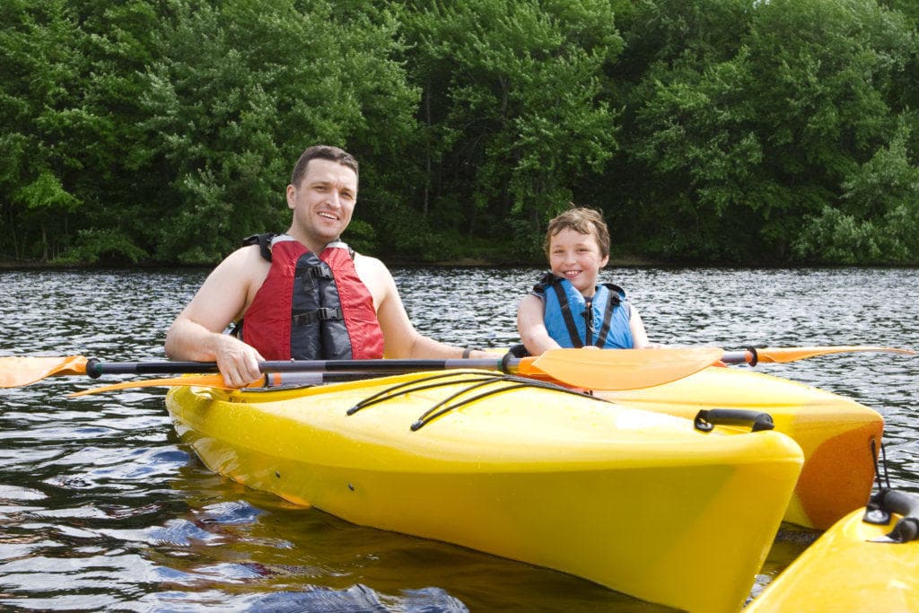 Father and child kayaking on calm river near wooded shoreline
