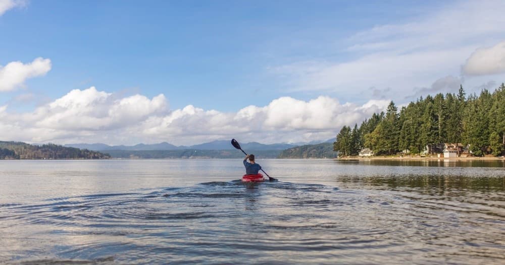 Kayaker paddling on scenic lake with forested shoreline