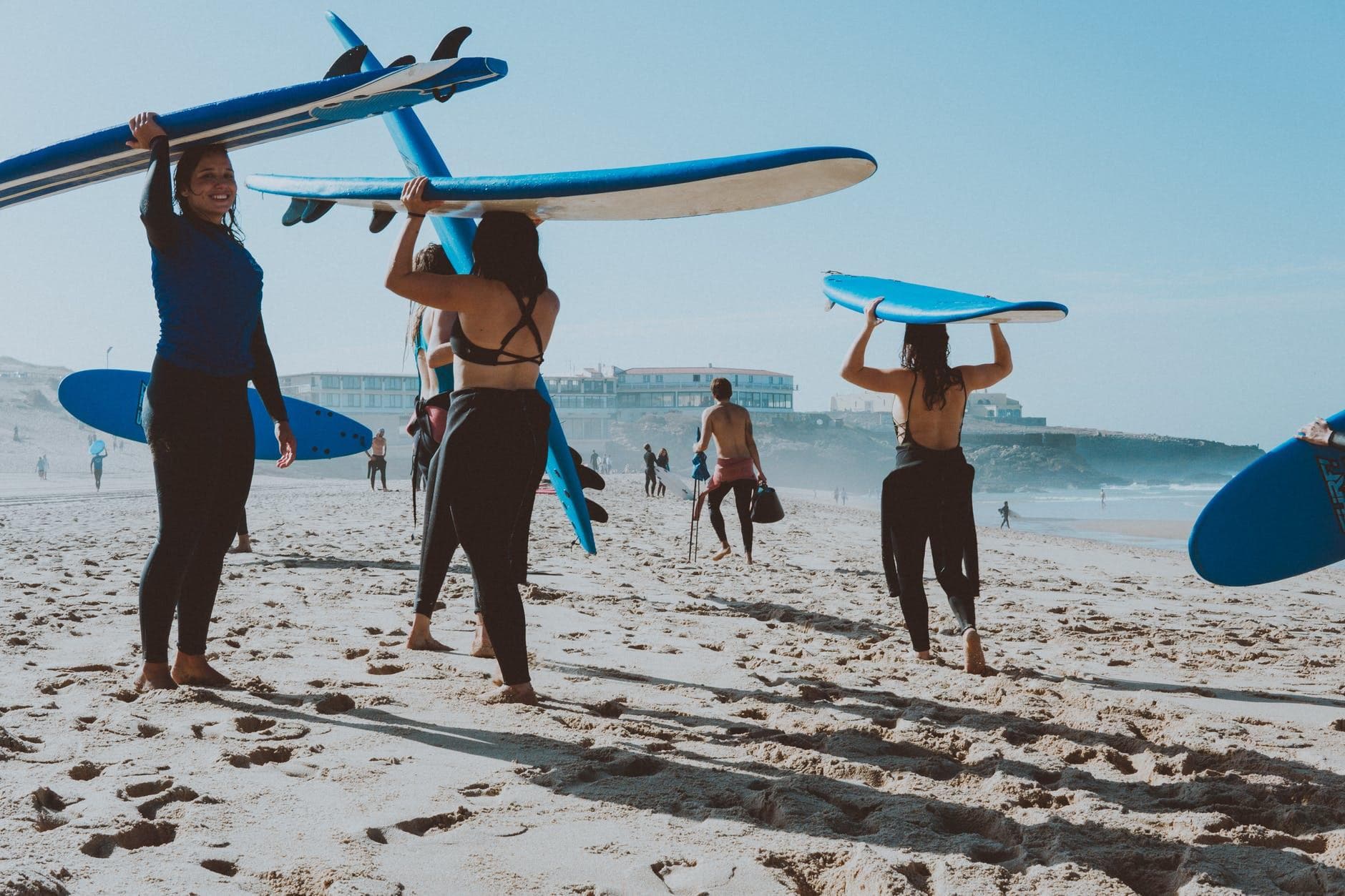 Group carrying surfboards across sunny beach heading to surf