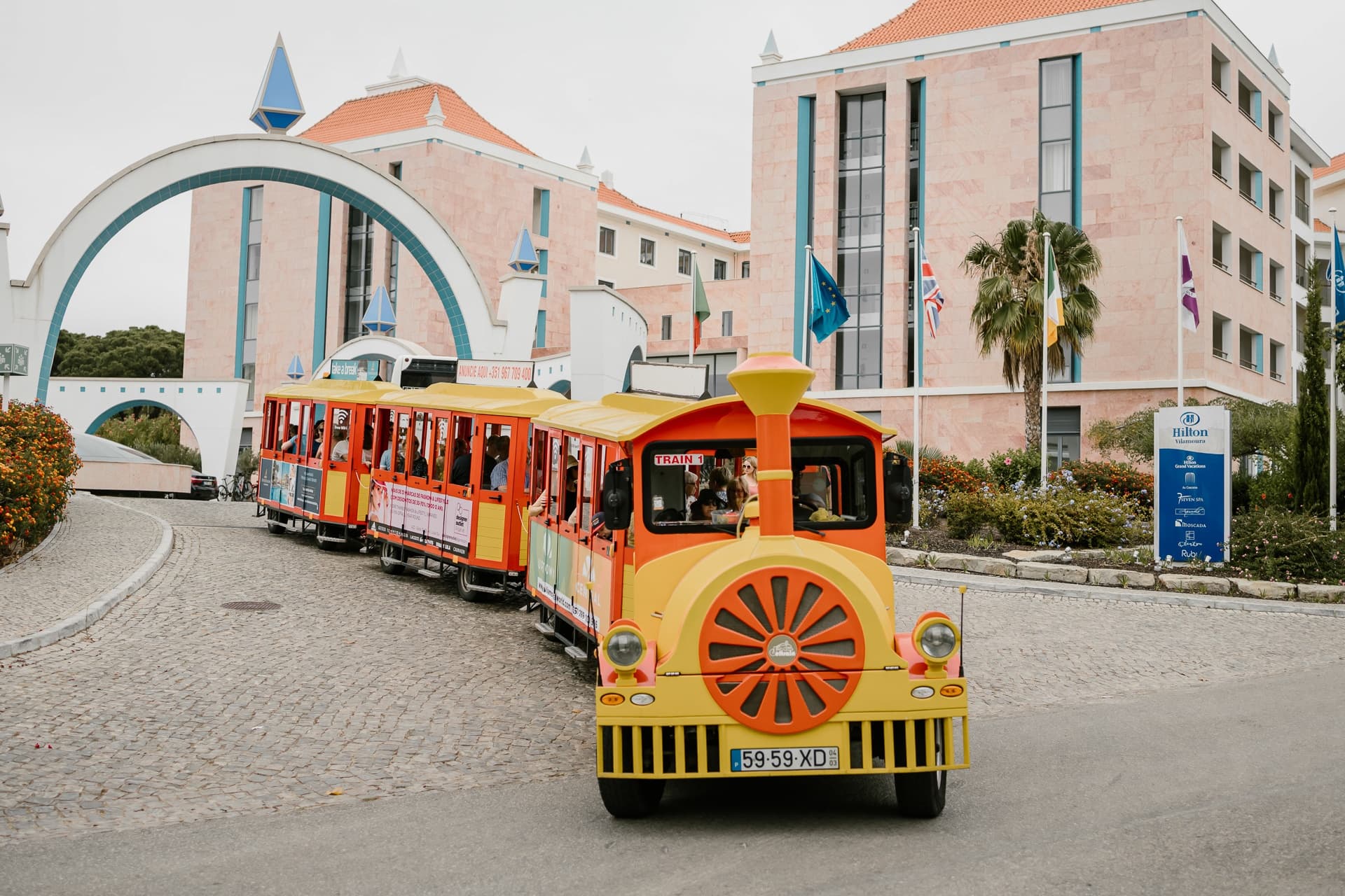 Bright yellow sightseeing train approaching resort archway, coastal town