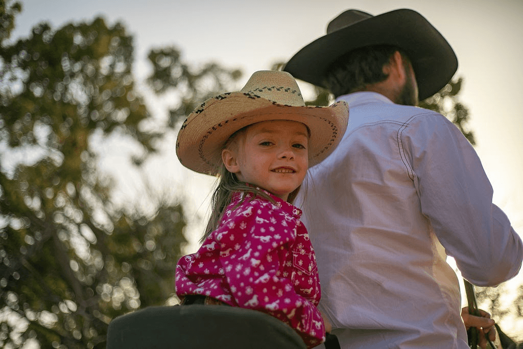 Child smiling on horseback with cowboy hat during sunset trail