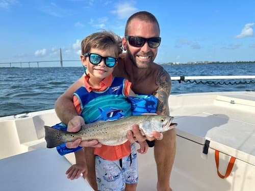 Dad and child holding spotted trout on sunny bay boat