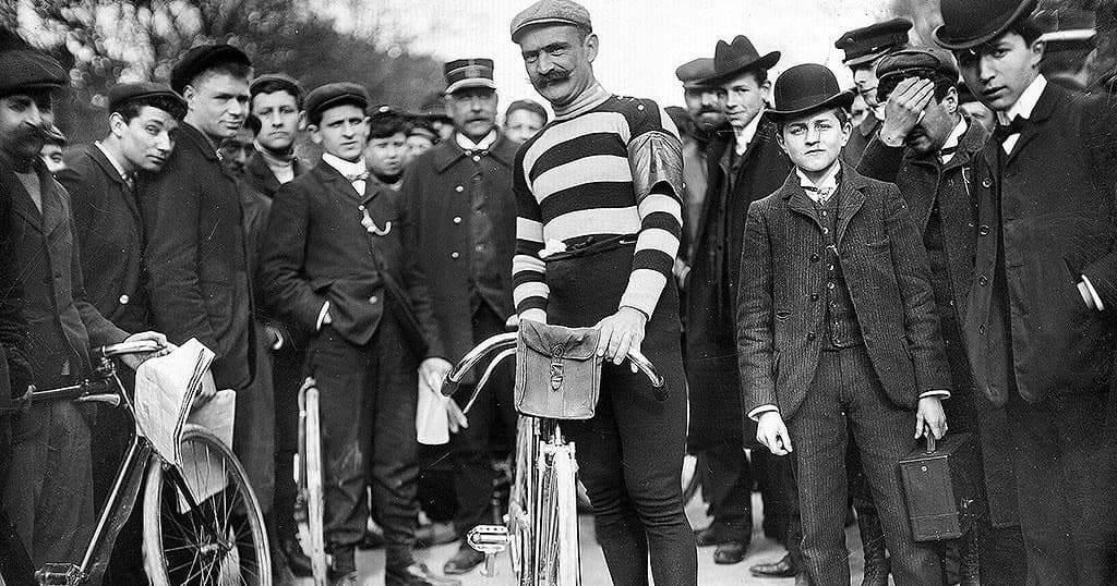 Cyclist posing with bicycle amid crowd at historic street race