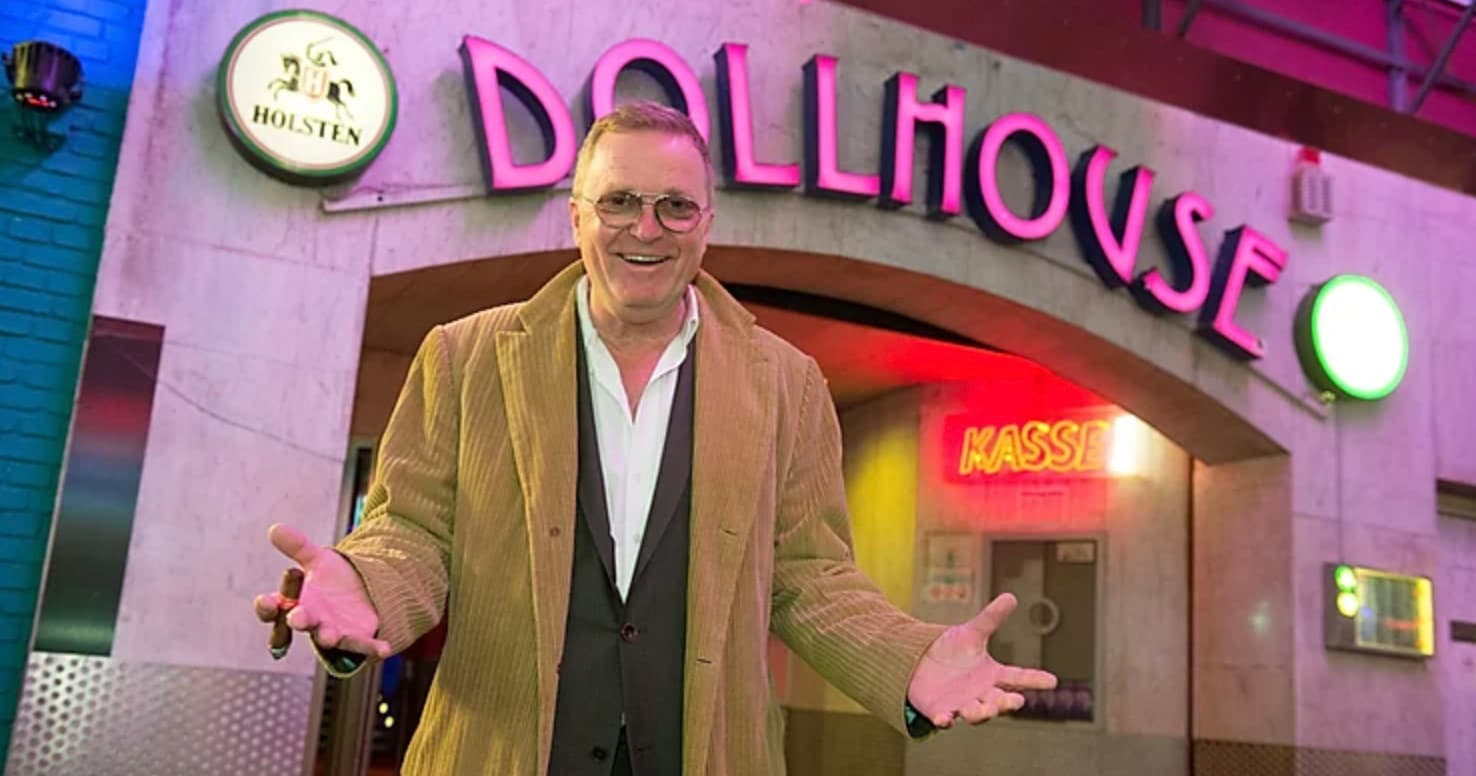 Person standing outside neon-lit Dollhouse club entrance at night