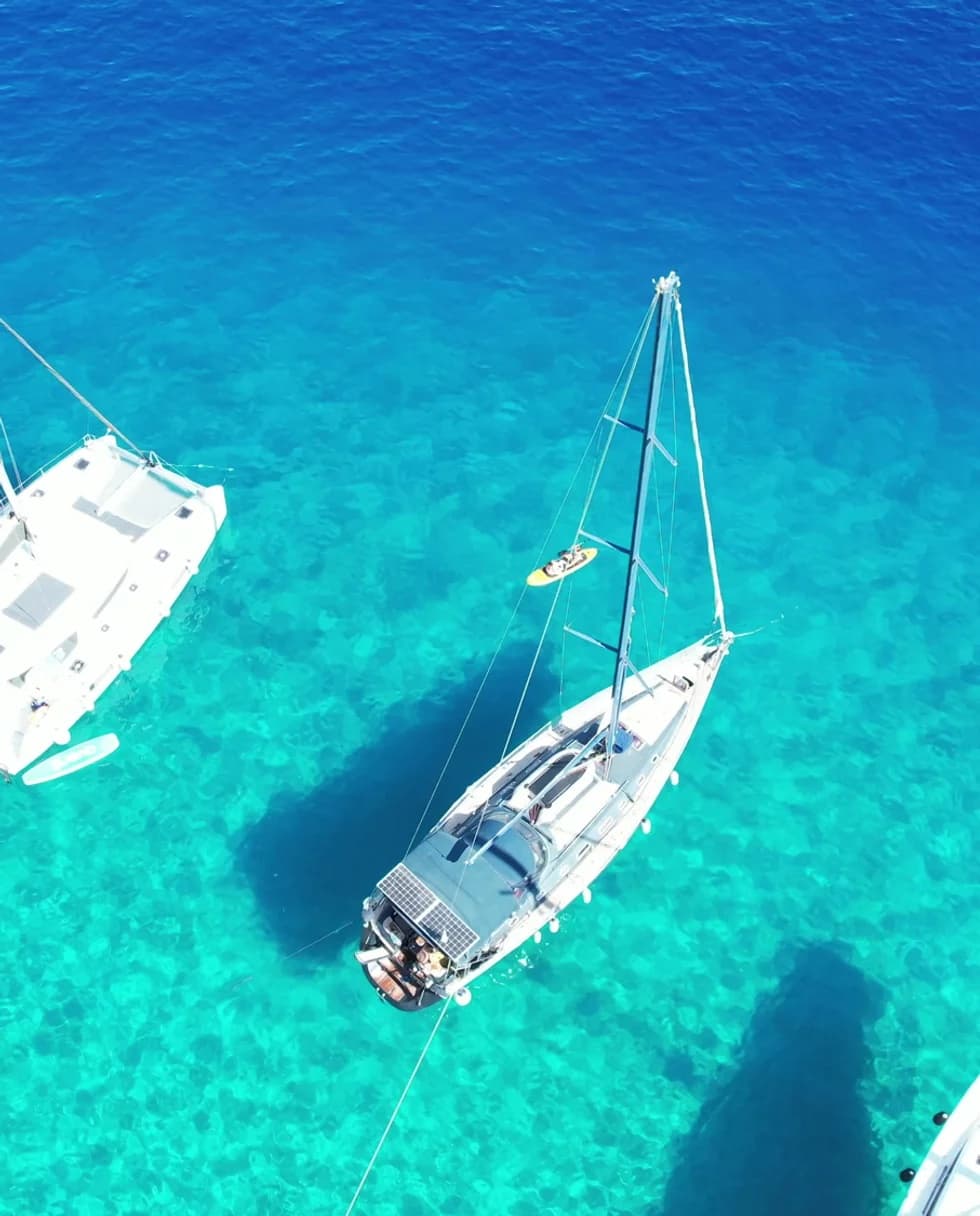 Aerial view of a sailboat in clear turquoise water, anchored