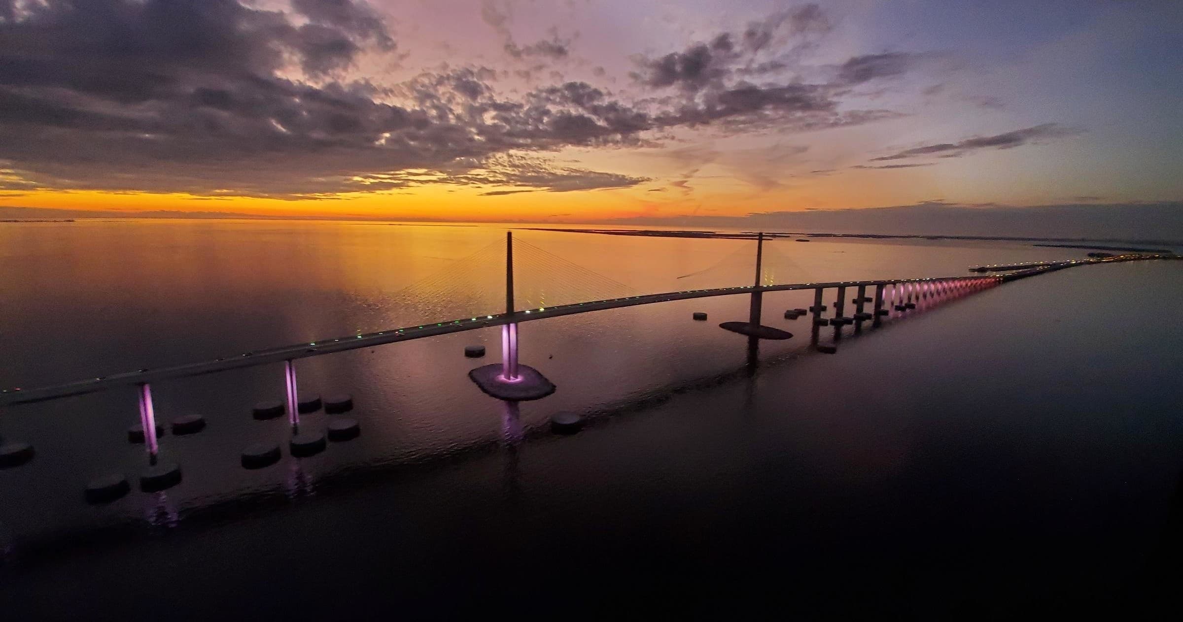 Golden sunset over coastal bridge with calm water aerial view
