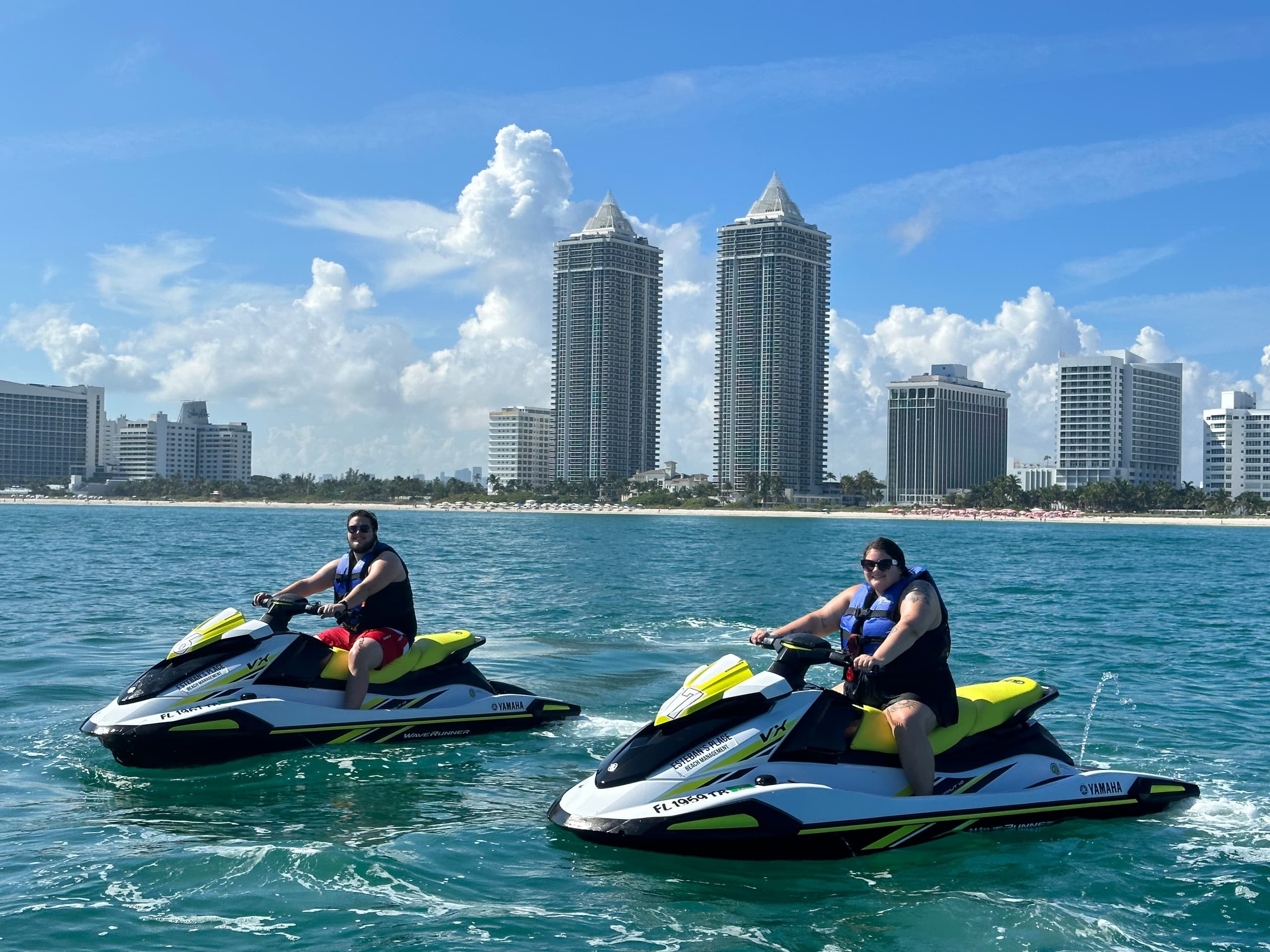 Two riders on jet skis cruising coastal waters near city skyline