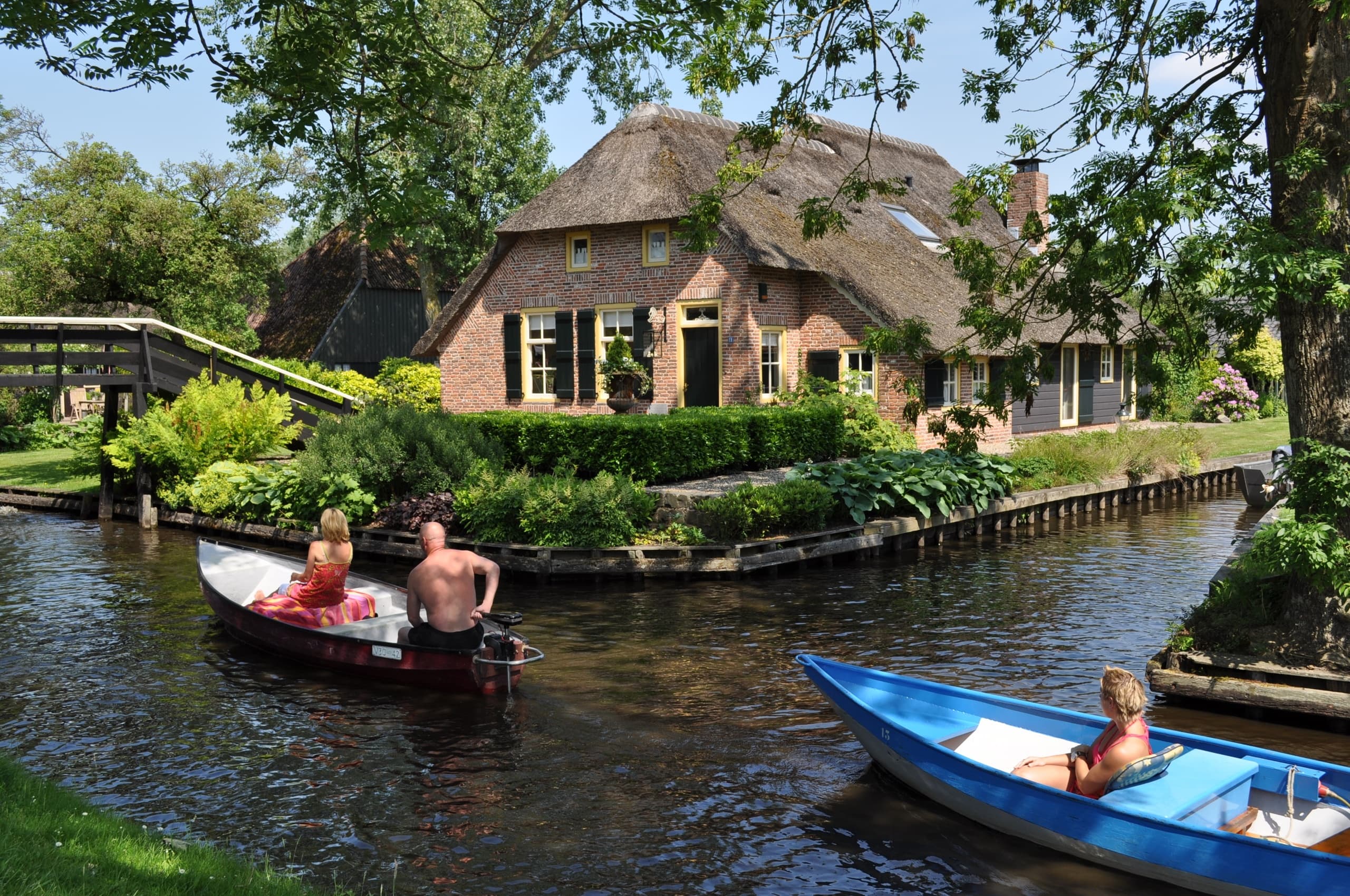Small leisure boats cruising past thatched houses on canals