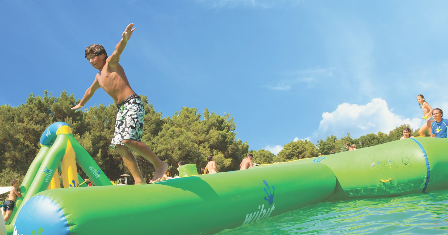 Person balancing on inflatable waterpark log on sunny lake shore