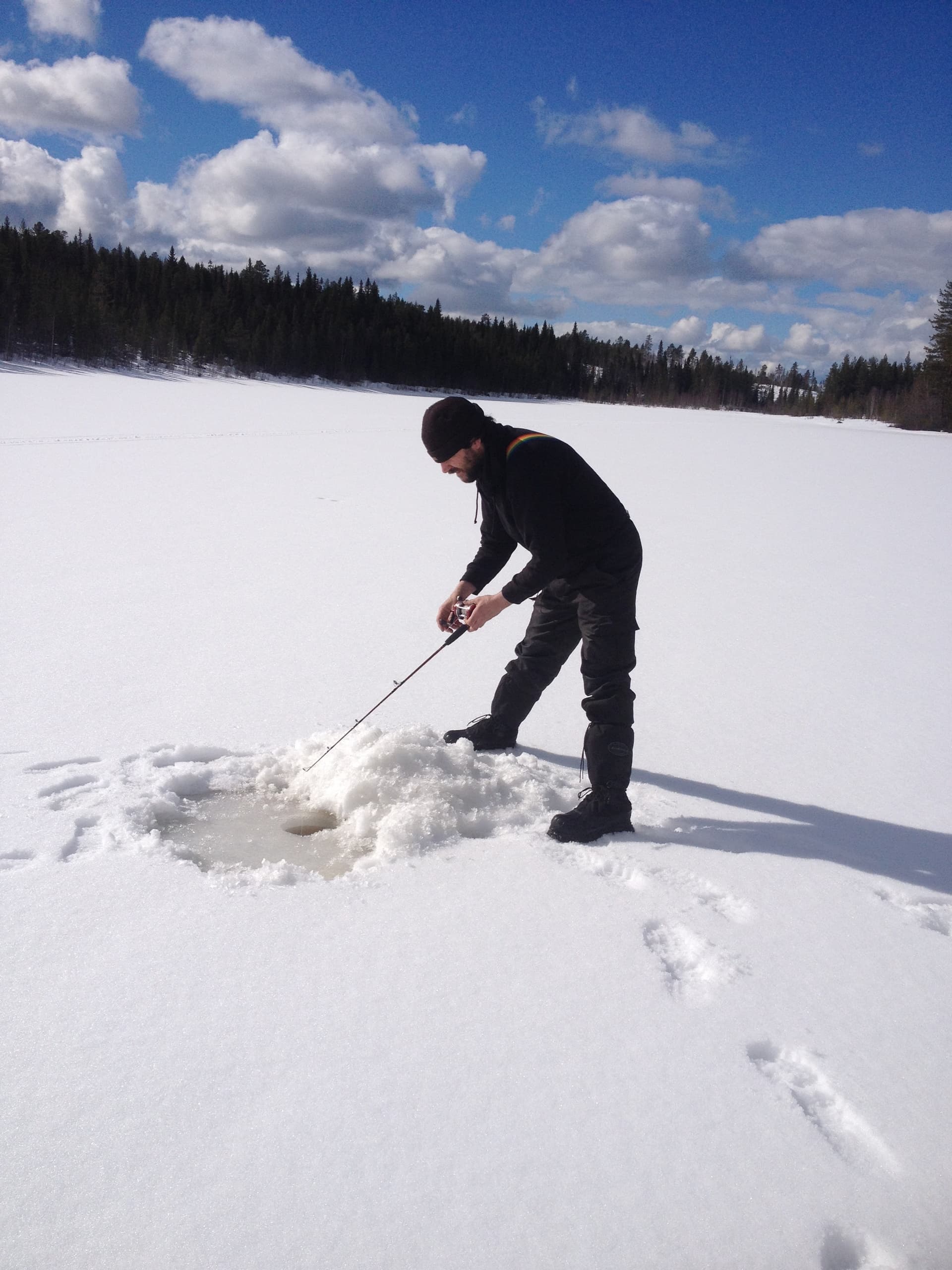 Angler ice fishing on frozen lake, drilling hole and casting