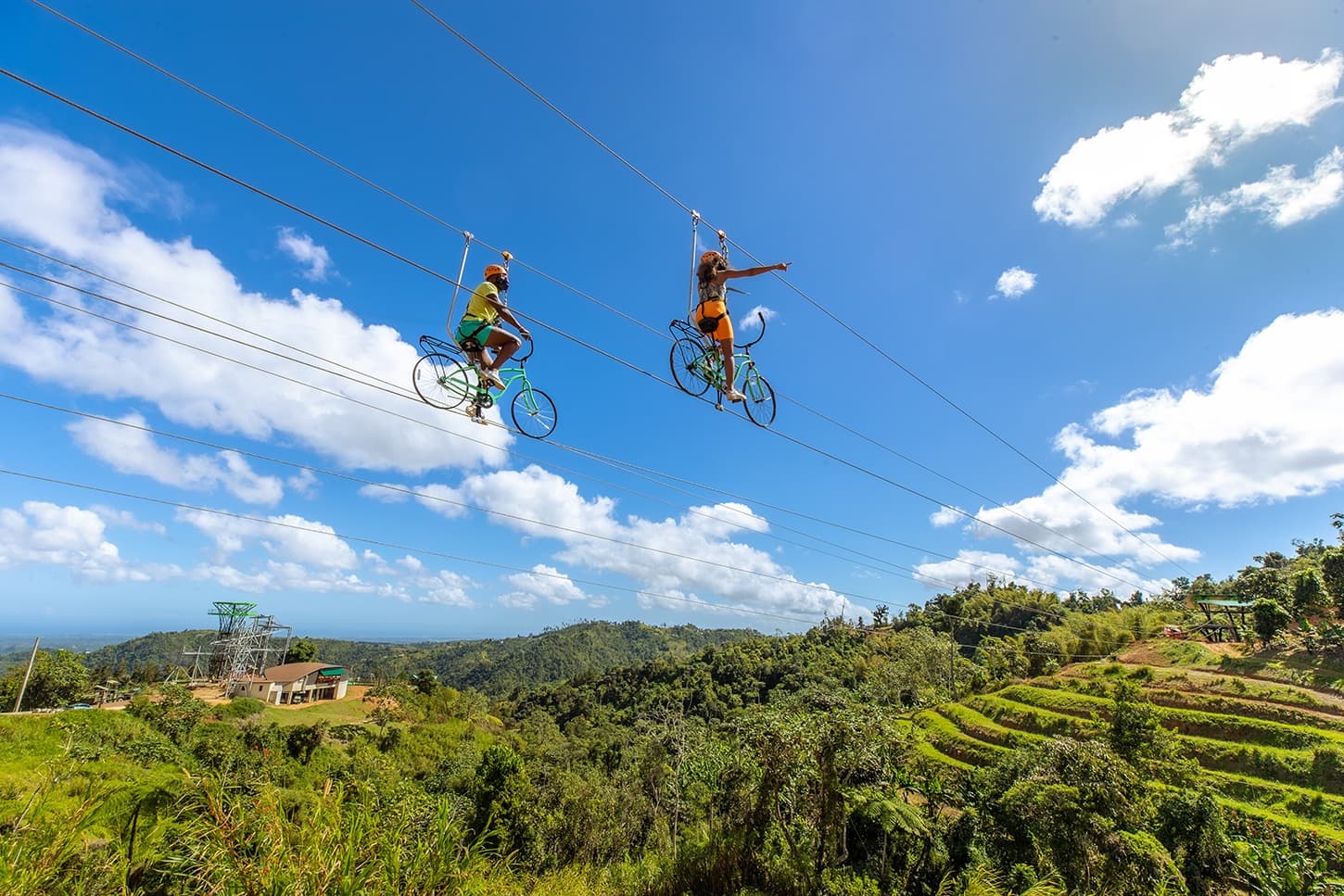 Two riders pedaling sky bicycle zipline across blue sky vistas