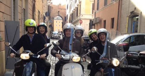 Friends riding Vespa scooters through historic Rome streets