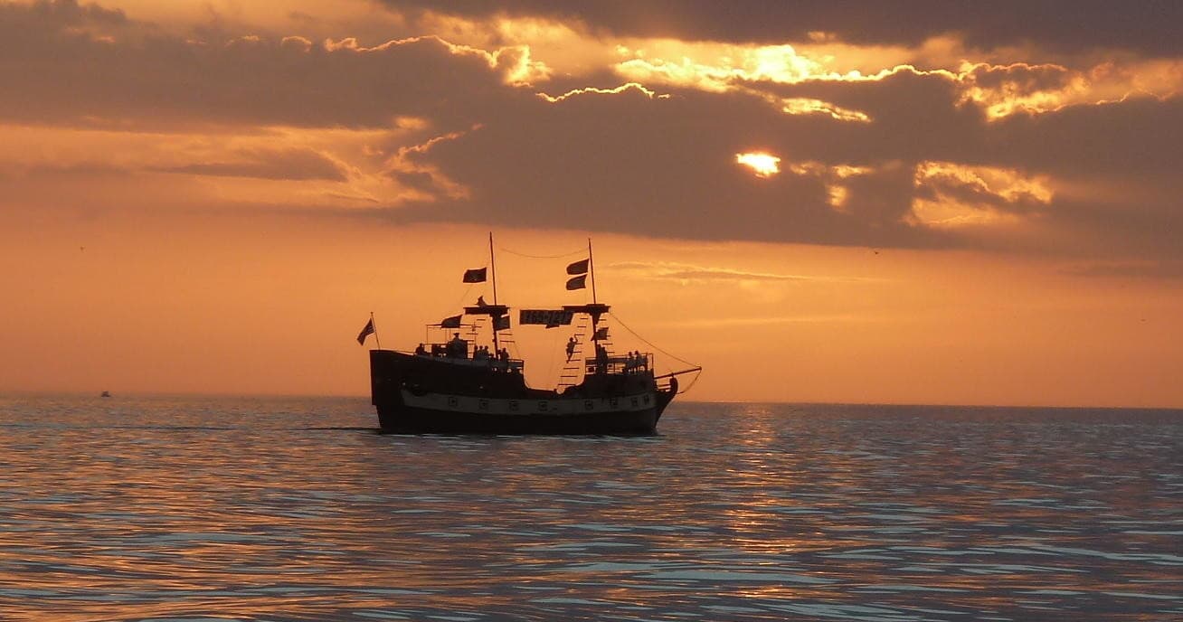 Orange sunset with small tour boat on calm Gulf waters off coast