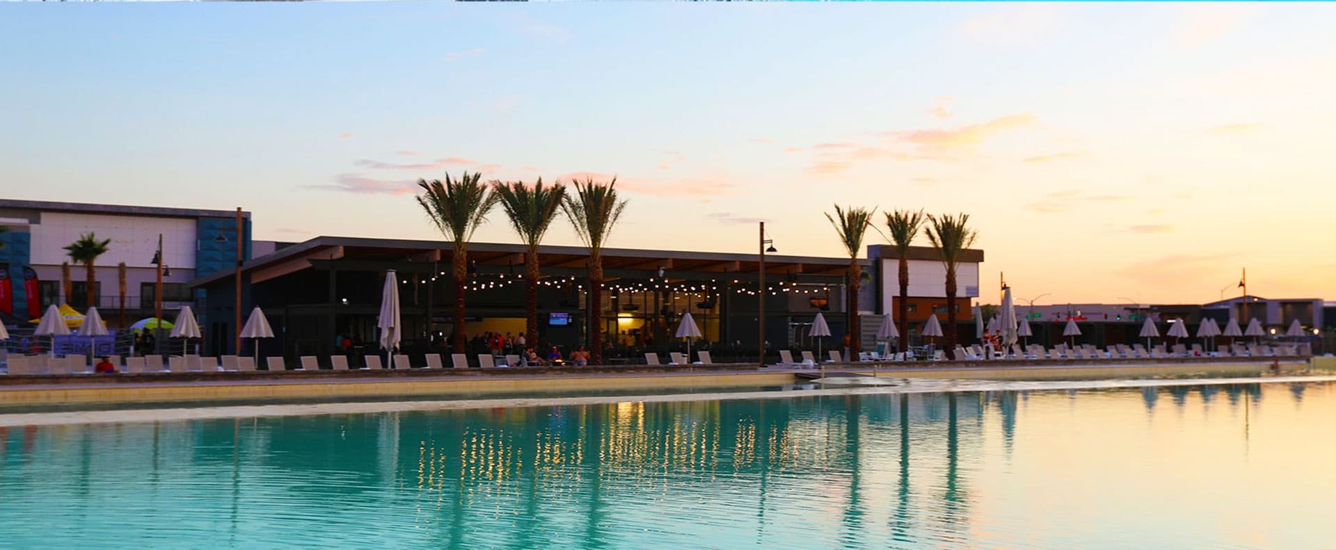 Sunset view of surf lagoon and palm trees at coastal surf park