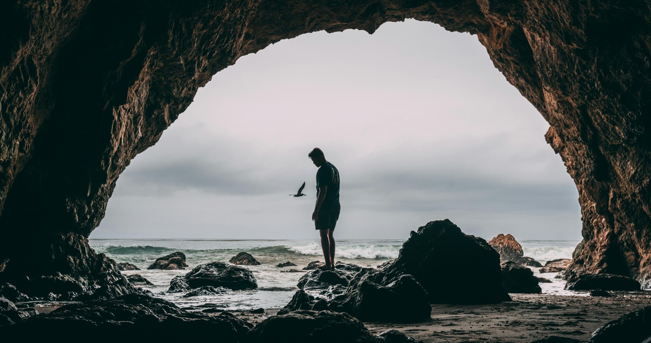 Person exploring sea cave on rocky Pacific shoreline at low tide