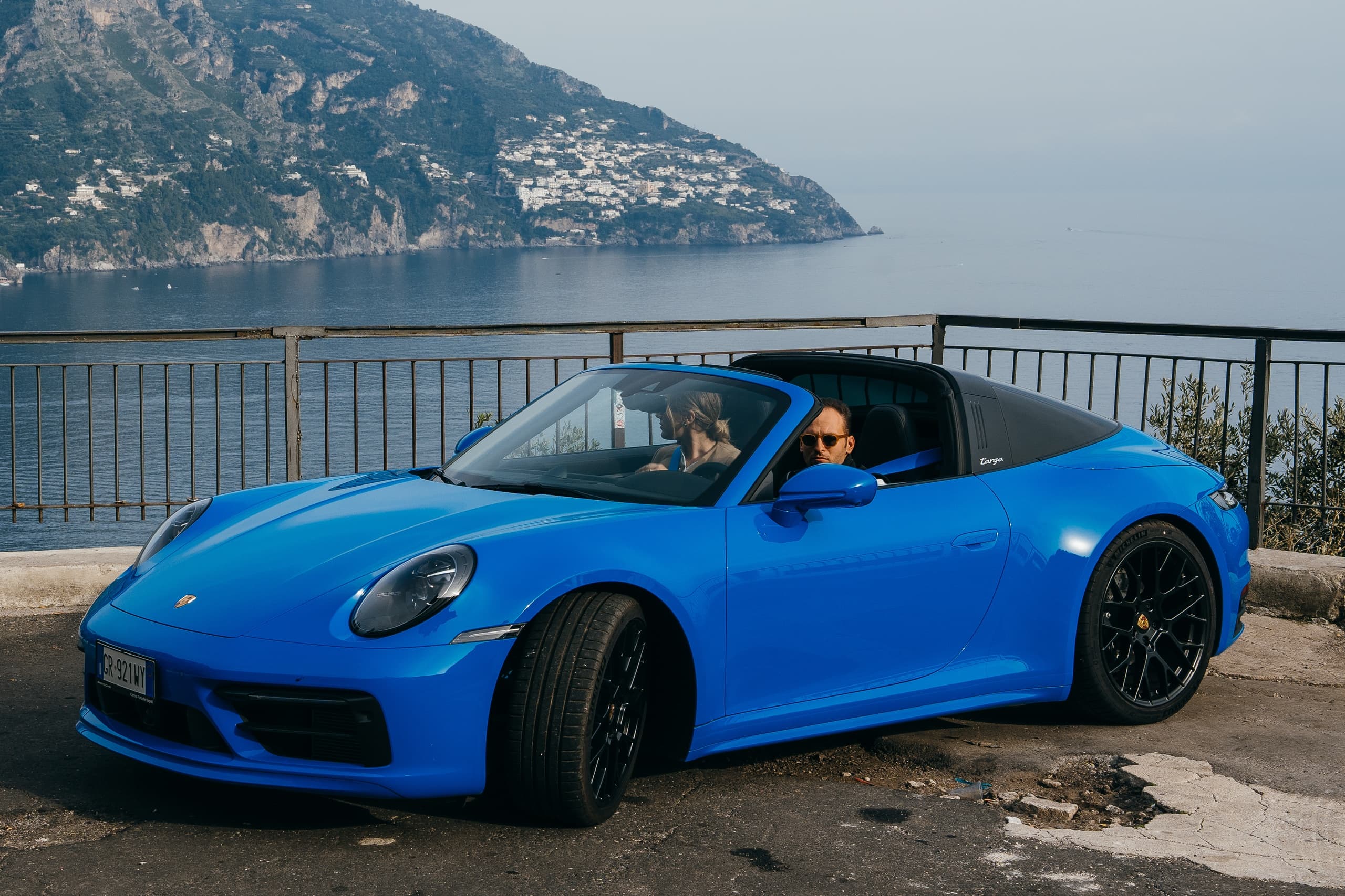 Blue sports car parked on coastal cliff road overlooking Amalfi Coast