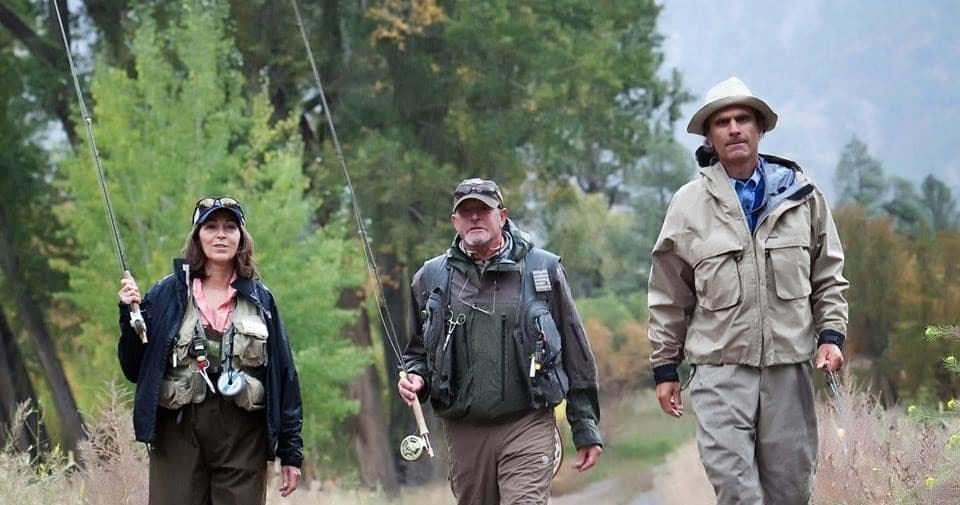 Group fly fishers hiking river trail with rods in mountain woods
