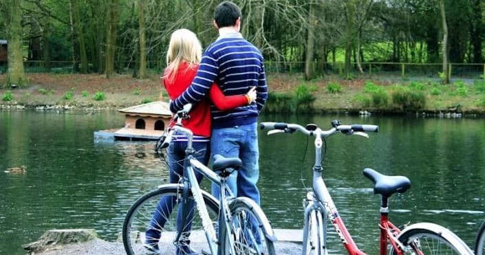 Couple embracing by lake with bikes amid Kilkenny woodland