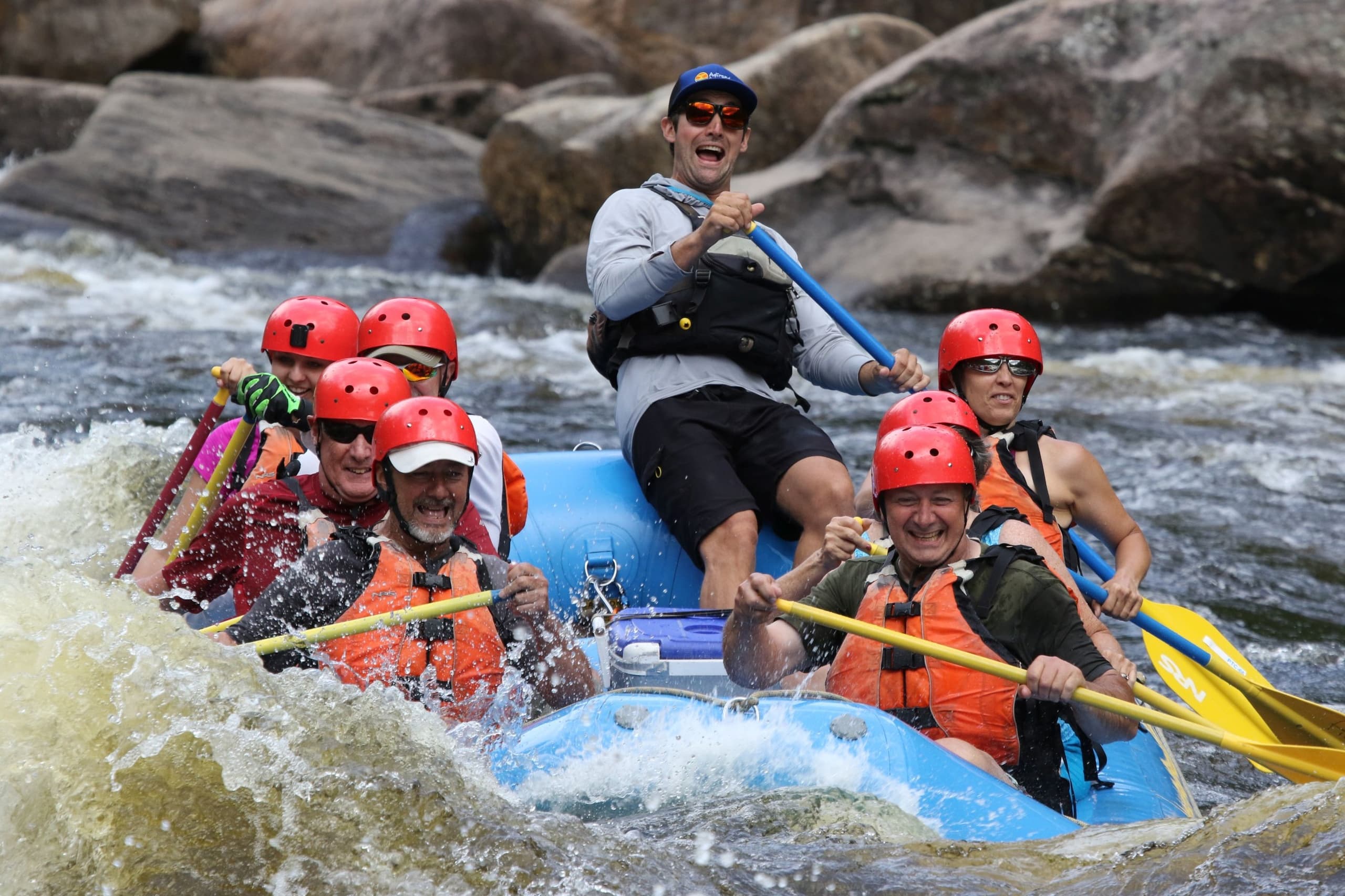 Group whitewater rafting with guide over rocky Adirondack rapids